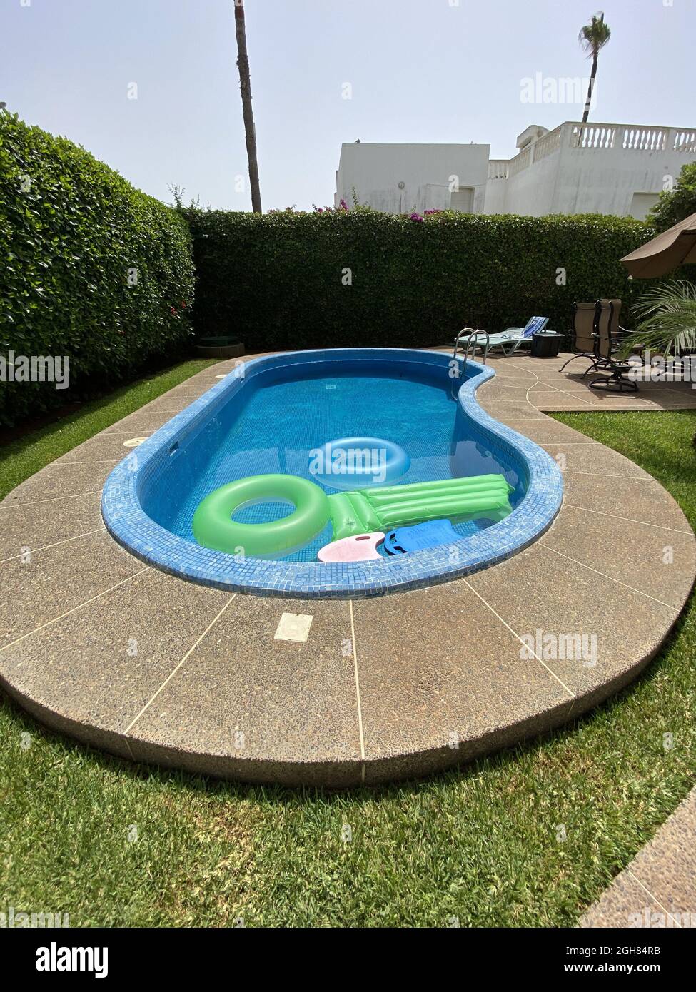 Piscine extérieure avec flotteurs verts et bleus entourés d'une clôture en herbe Banque D'Images