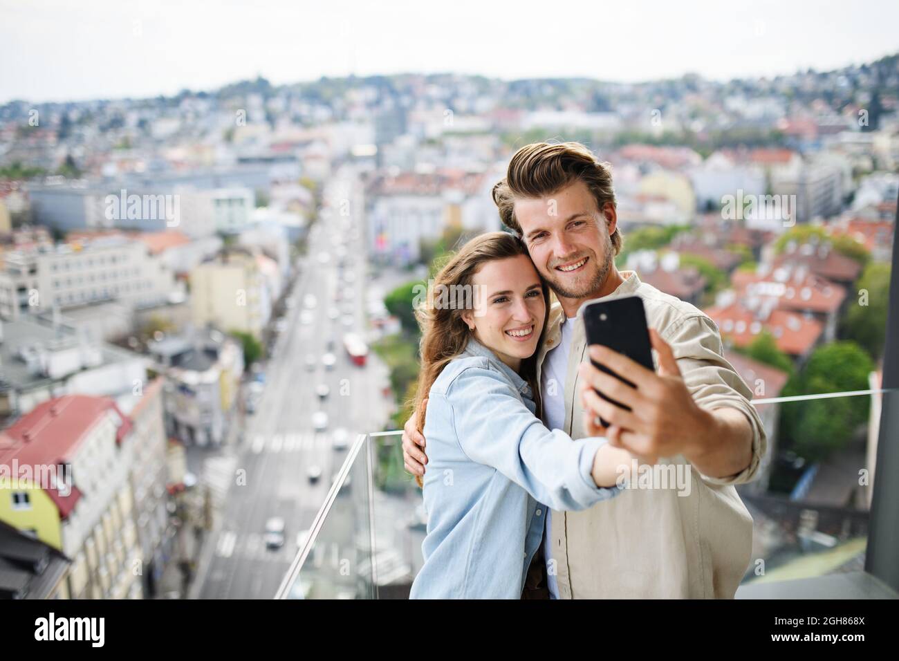 Joyeux jeune couple amoureux debout à l'extérieur sur le balcon à la maison, emportant le selfie avec un smartphone. Banque D'Images