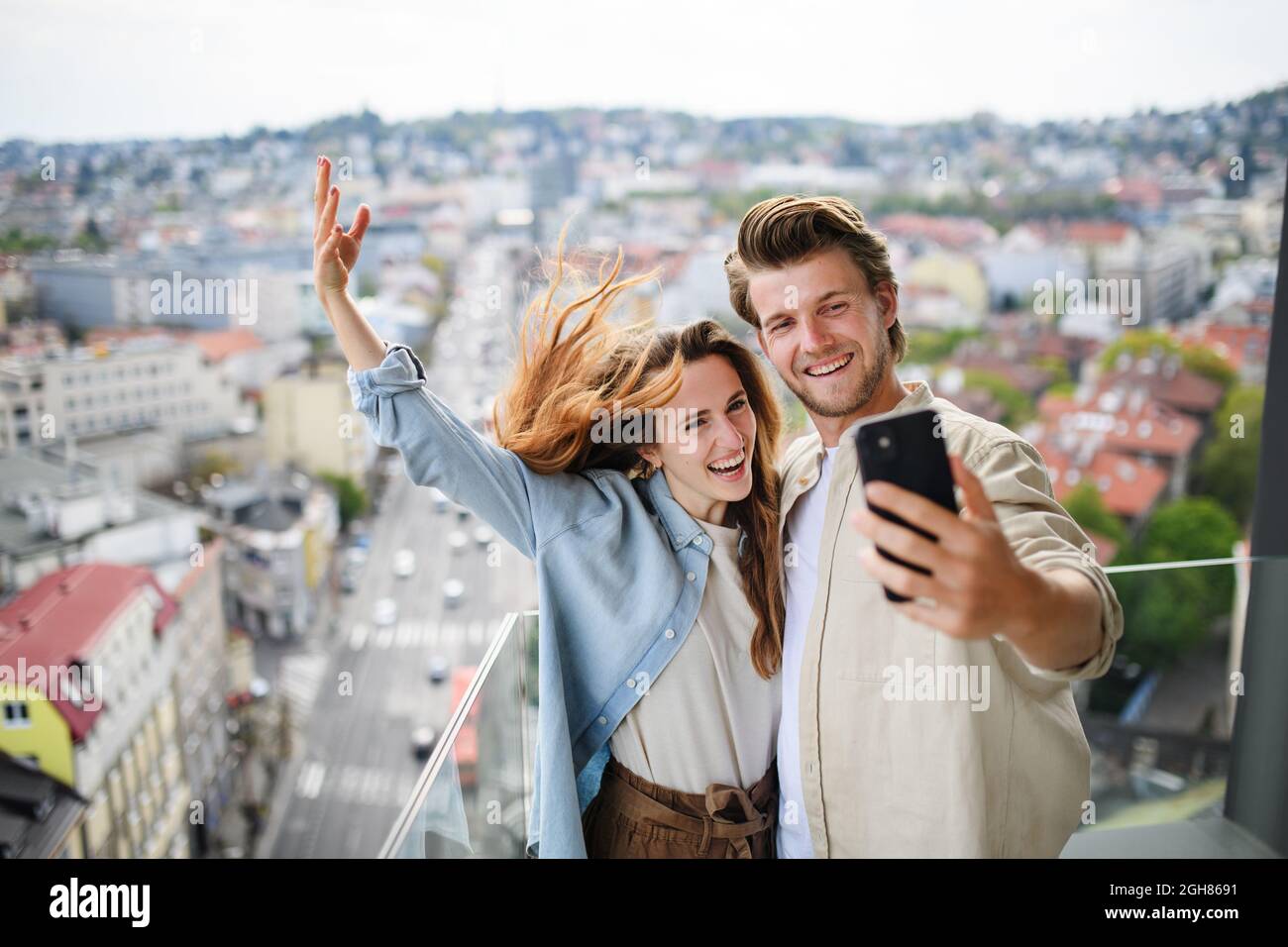 Joyeux jeune couple amoureux debout à l'extérieur sur le balcon à la maison, emportant le selfie avec un smartphone. Banque D'Images