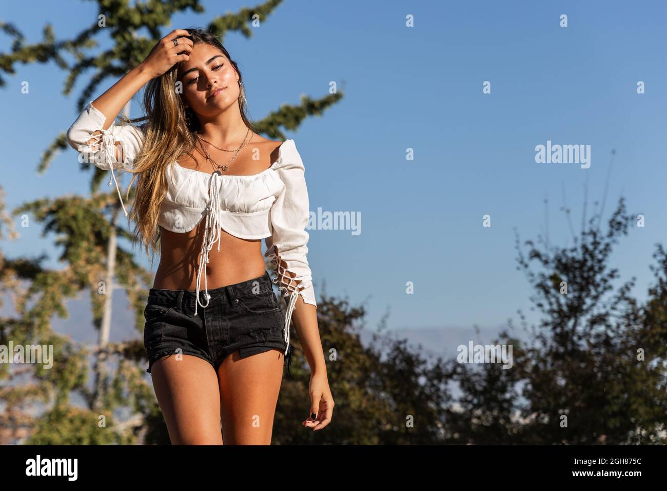 Jolie femme hispanique portant un haut à manches longues et un short à l'épaule lors d'une partie en plein air Banque D'Images