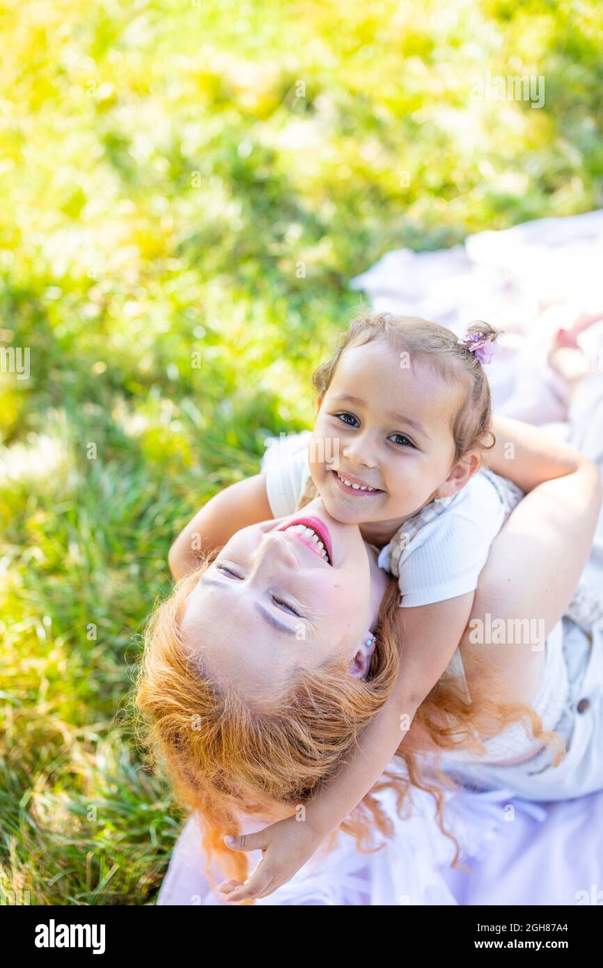 Maman et fille riant et embrassant assis sur une couverture dans le parc le concept d'une famille heureuse, amitié, et amour. Banque D'Images