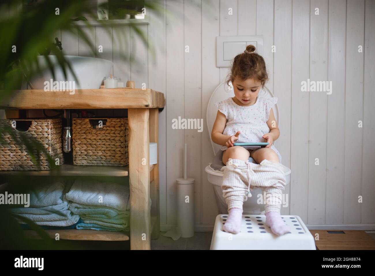 Portrait de mignon petit assis sur les toilettes à l'intérieur à la maison, à l'aide d'un smartphone. Banque D'Images