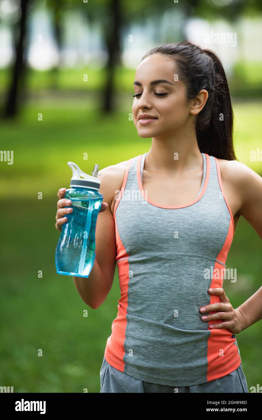 une femme heureuse et ajustée tenant un biberon de sport debout avec la main sur la hanche Banque D'Images