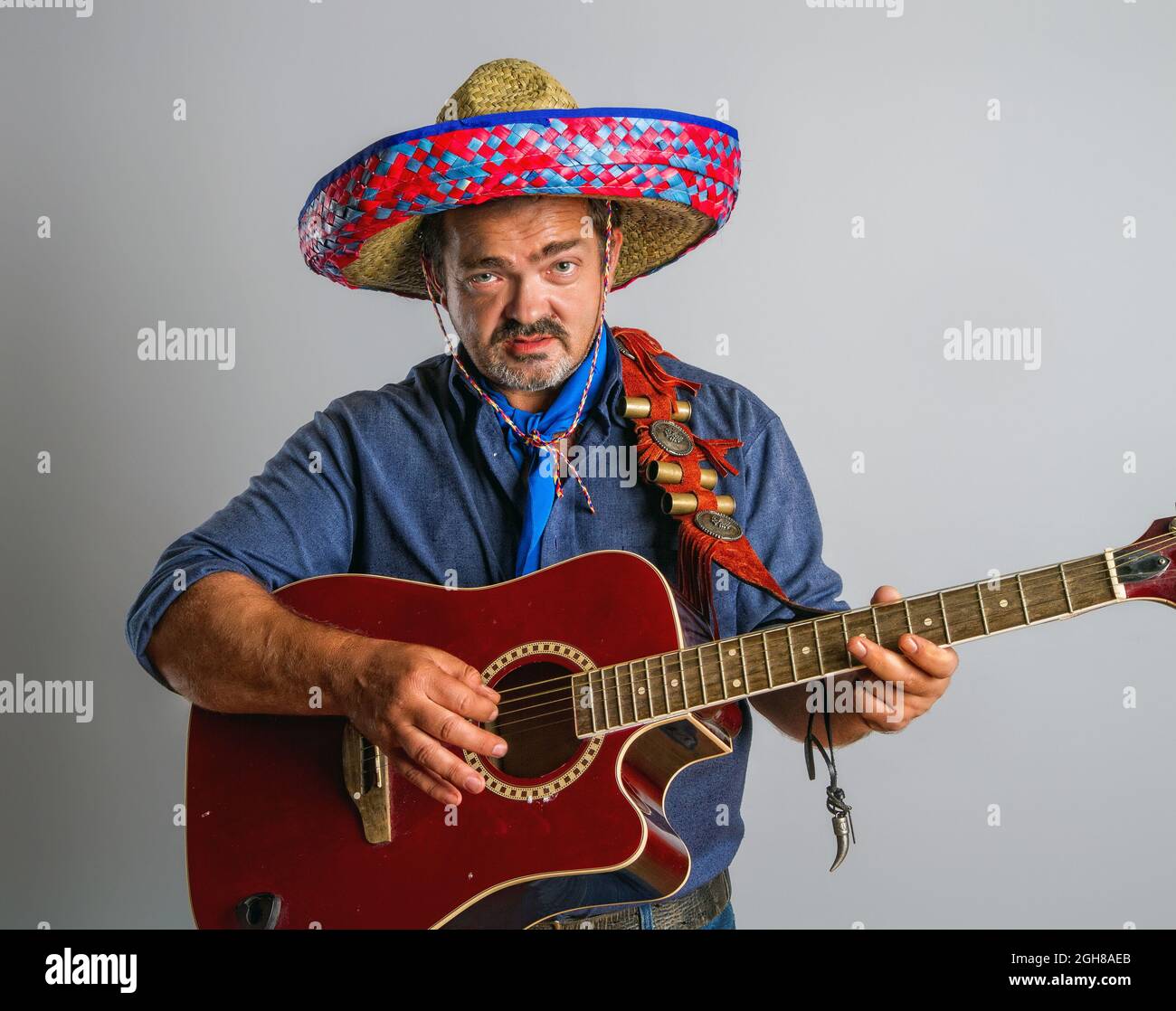 Un homme mexicain émotif adulte dans la hauteur nationale de sombrero joue de la guitare sur fond gris Banque D'Images