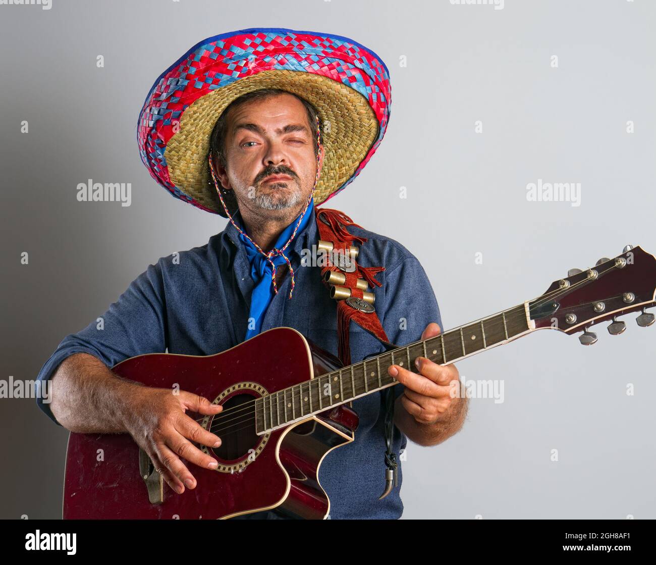 Un homme mexicain émotif adulte dans la hauteur nationale de sombrero joue de la guitare sur fond gris Banque D'Images