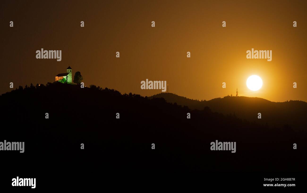 La lune de la fraise du 24 juin 2021 s'élève à côté de l'église de Saint Ana et du mont Krim sur les Maures de Ljubljana en Slovénie. Banque D'Images