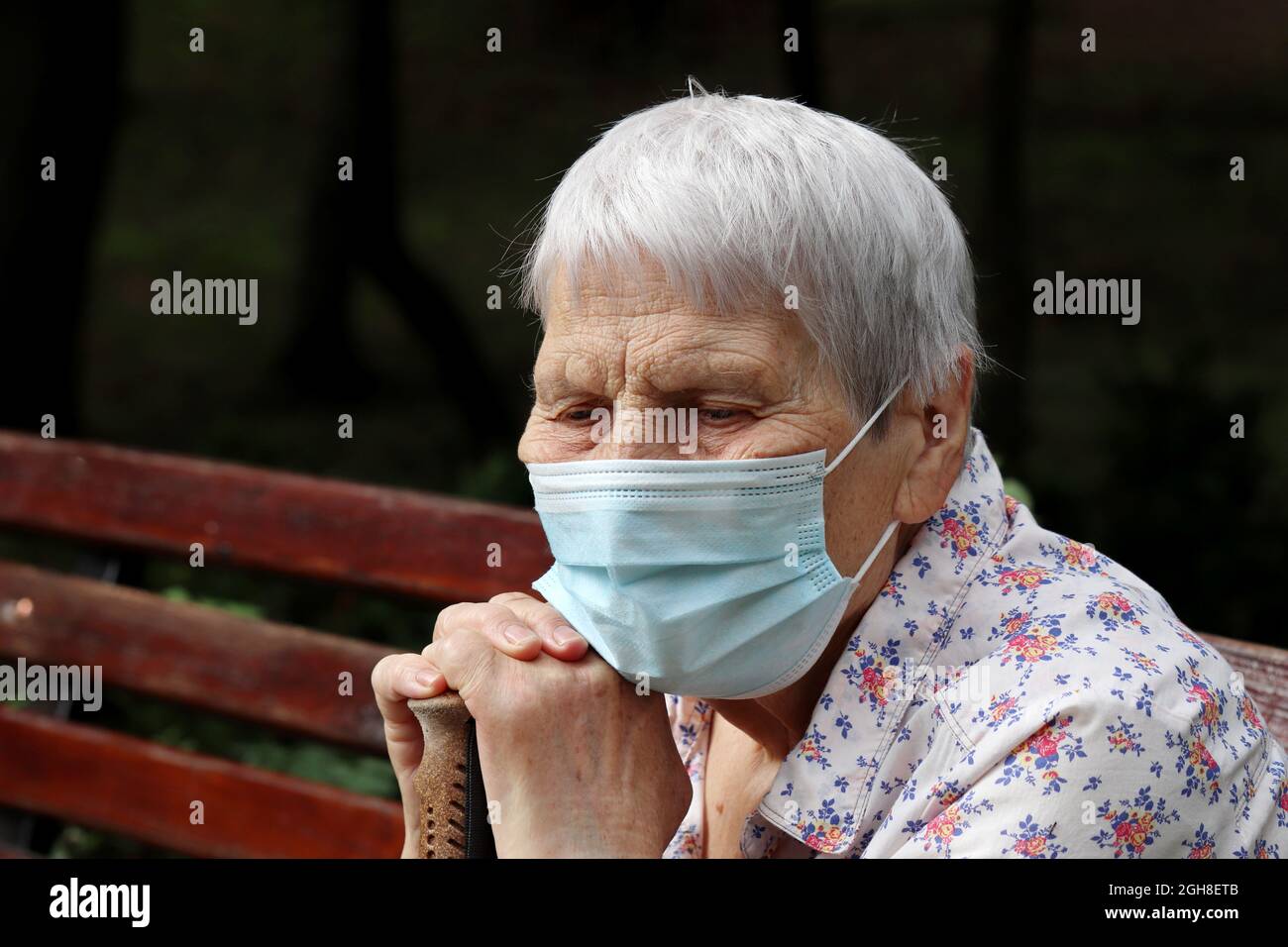 Vieille femme dans un masque de protection assise sur un banc dans le parc. Sécurité pendant la pandémie du coronavirus, la vie à la retraite Banque D'Images