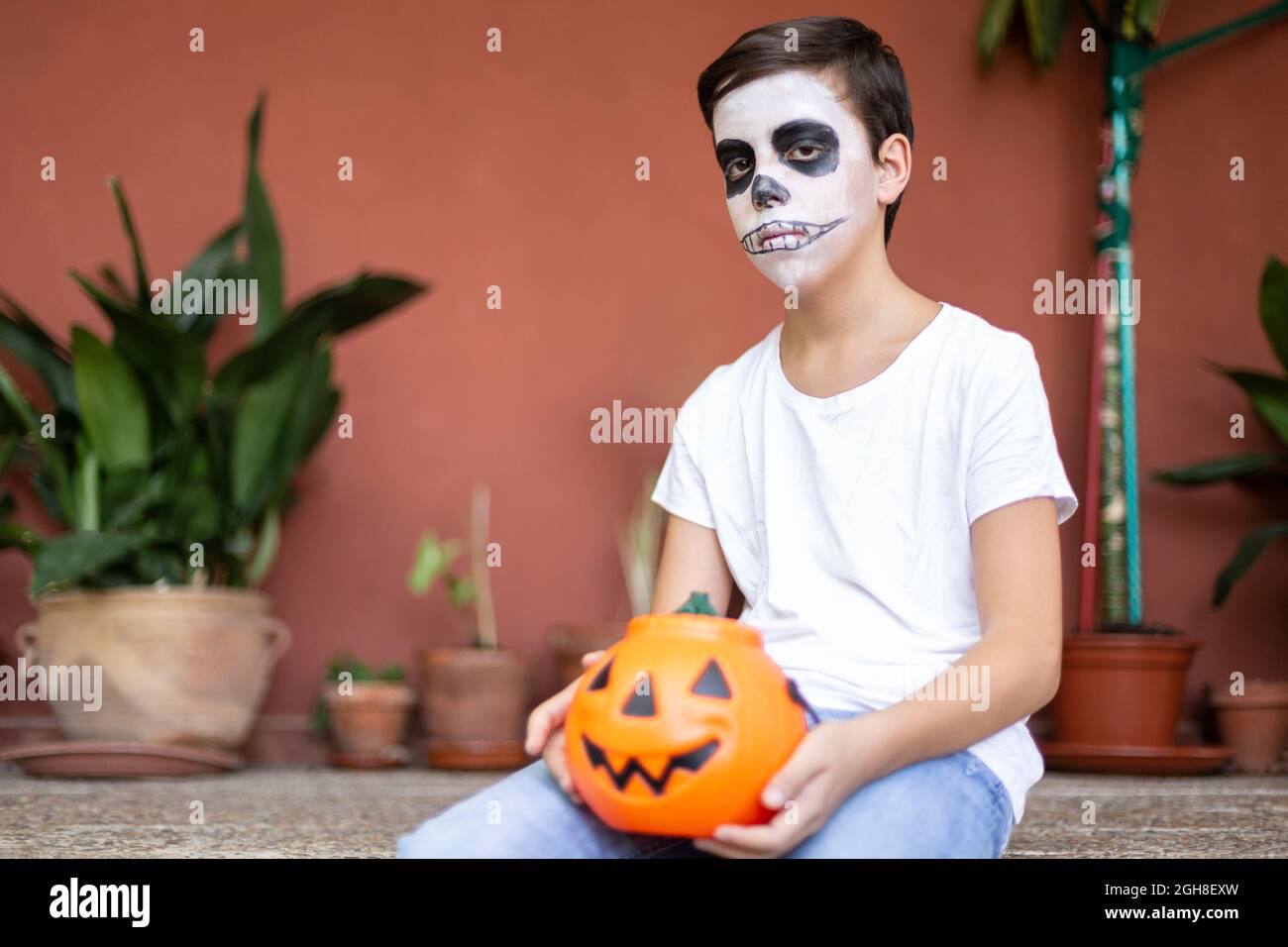 Garçon assis à l'entrée de sa maison. Il est sérieux et avec maquillage comme un crâne pour la célébration d'Halloween. Espace pour le texte. Banque D'Images