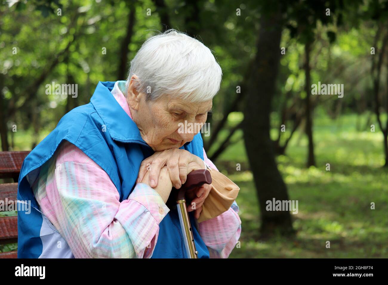 Femme âgée assise avec une canne à pied et retirée d'un masque médical sur un banc dans un parc. Un mode de vie sain à la vieillesse, la vie à la retraite Banque D'Images