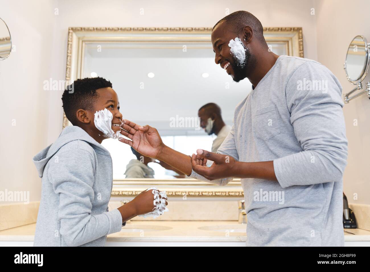 Père afro-américain avec son fils s'amusant avec de la mousse à raser dans la salle de bains Banque D'Images