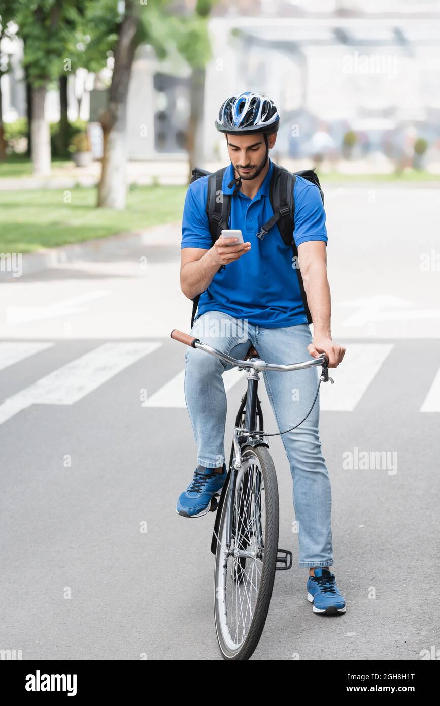 Homme de livraison arabe avec sac à dos en utilisant un smartphone tout en  faisant du vélo à l'extérieur Photo Stock - Alamy