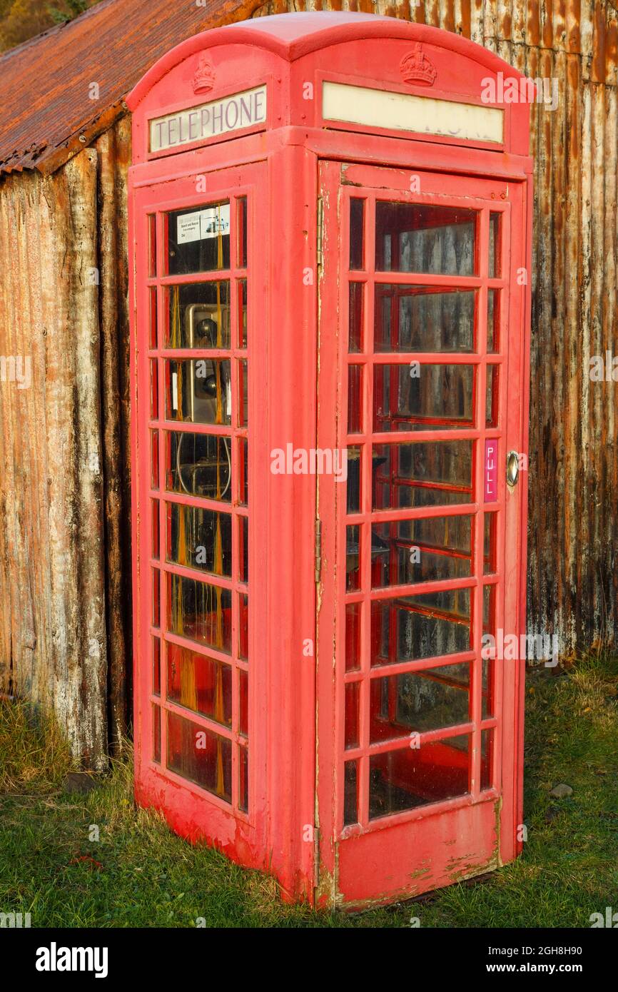 Une boîte téléphonique rouge abîmé se trouve à côté d'une cabane rouillée dans la campagne écossaise. Banque D'Images