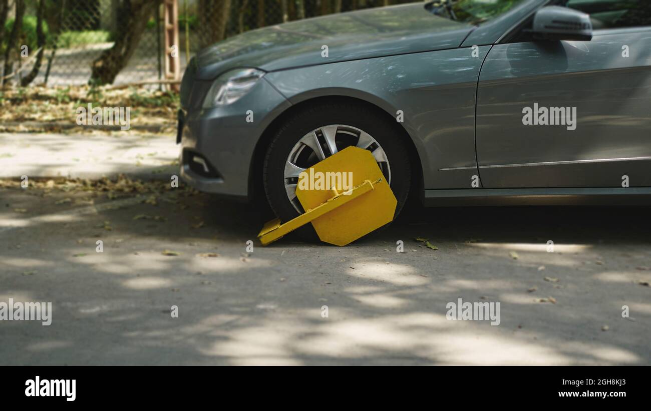Une voiture garée avec une serrure à pneu jaune pour la violation de stationnement illégal. Zone de blocage des roues restreinte pour le stationnement. Banque D'Images