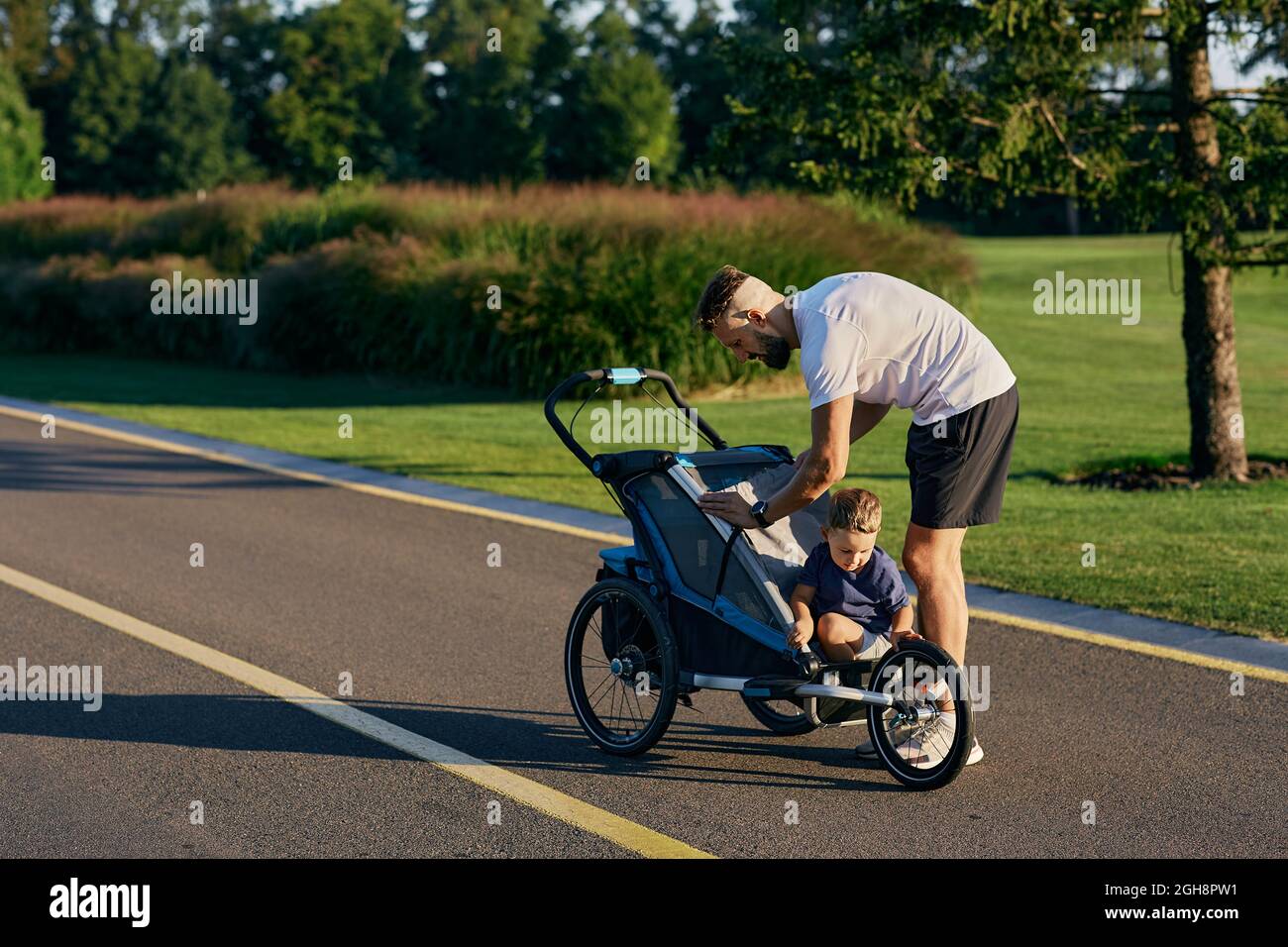 Père avec son petit fils avec poussette de jogging pendant l'entraînement du matin et courir dans le parc de la ville. Paternité, papa et enfant. Le jour du père Banque D'Images