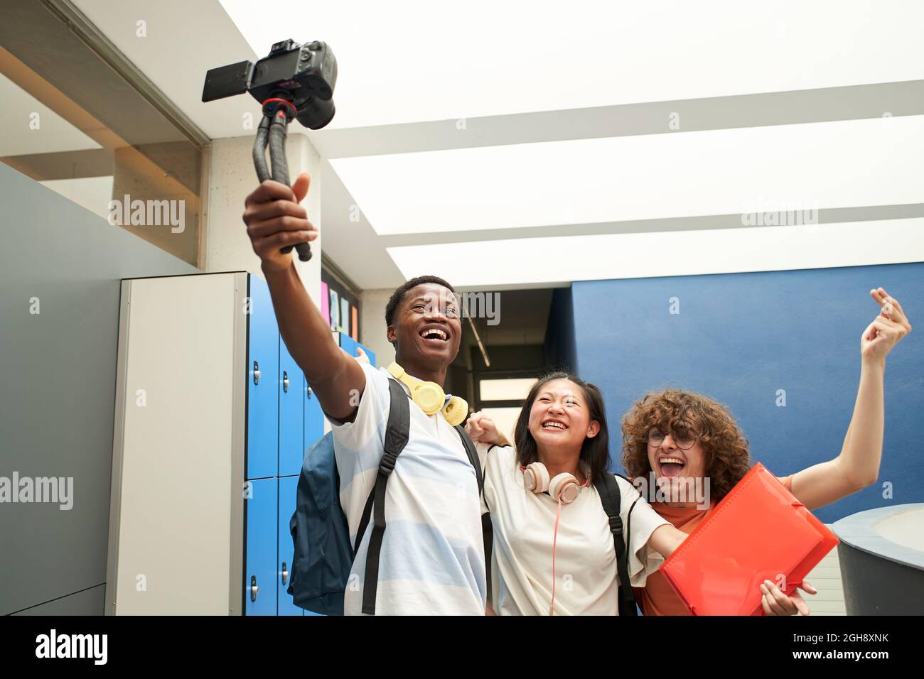Groupe d'élèves souriants blogging à l'école. Groupe multiethnique de jeunes enregistrant une vidéo avec une caméra professionnelle. Banque D'Images