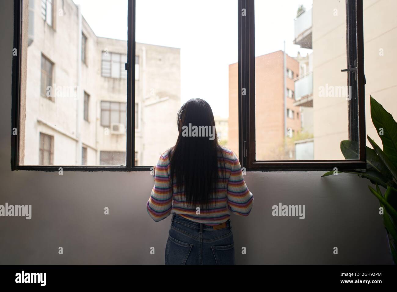 Vue arrière une fille africaine s'est penchée hors de la fenêtre, regardant à l'extérieur où il y a de grands bâtiments. Banque D'Images