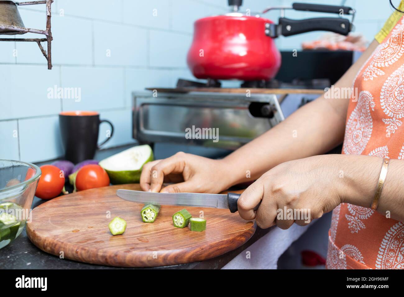 Gros plan d'une jeune femme indienne portant un tablier de cuisine et de coupe de légumes dans la cuisine domestique sur cuisinière à gaz Banque D'Images