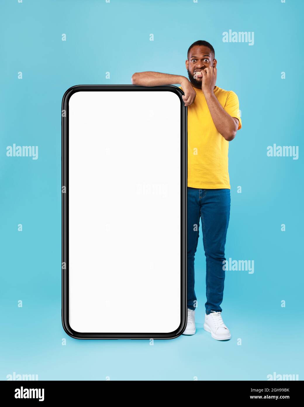 Un gars noir se penchant sur un smartphone géant avec écran vide, mordant des ongles dans la panique, peur de manquer la vente de magasin Web, mockup Banque D'Images