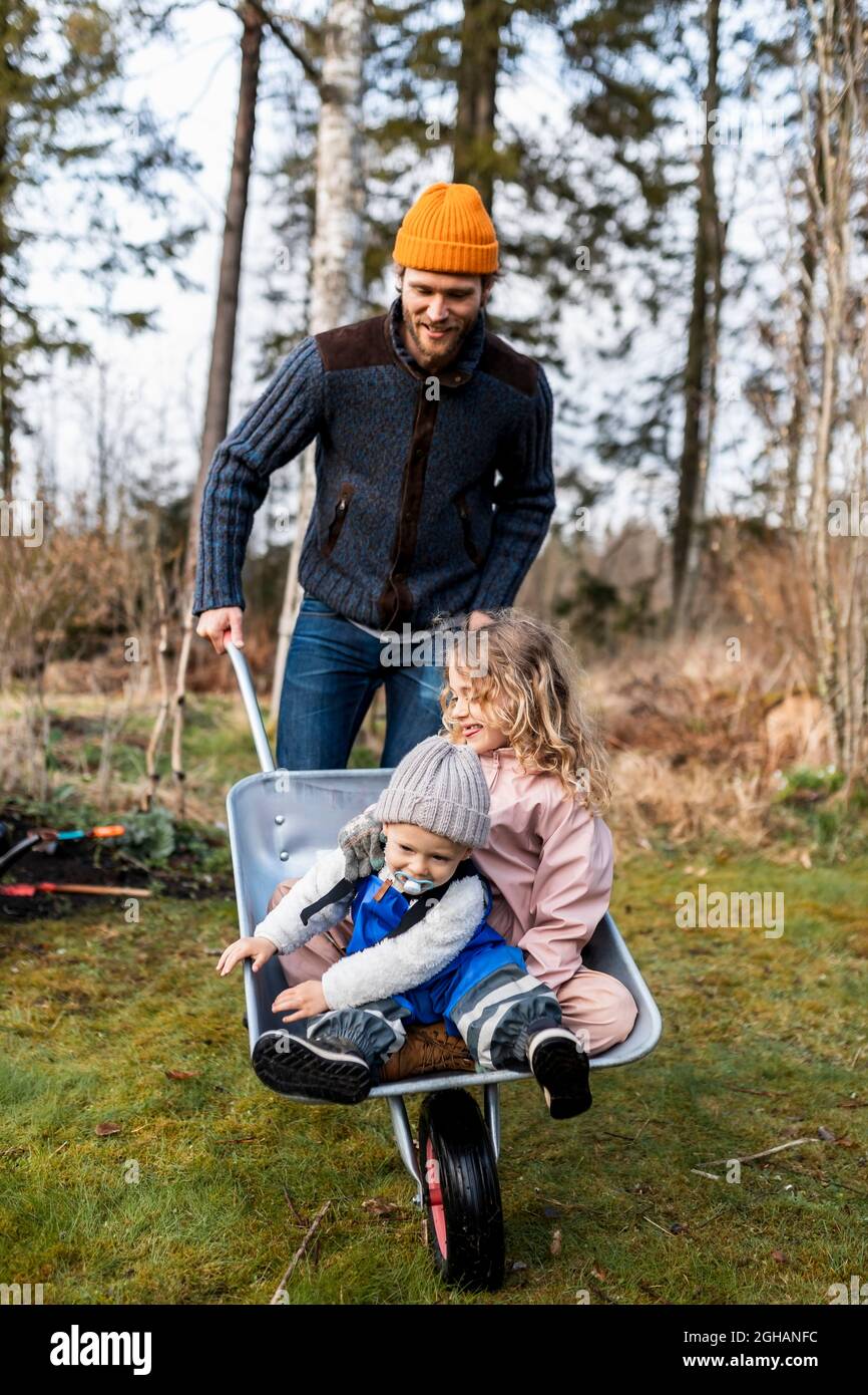 Un joueur qui fait rouler son fils et sa fille assis dans une brouette à l'arrière de la cour Banque D'Images