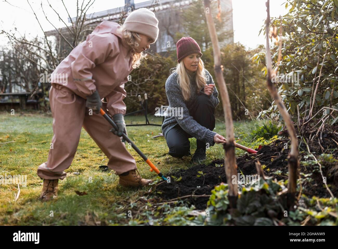 Pleine longueur de mère et fille creusant avec la pelle tout en faisant le jardinage à la cour arrière Banque D'Images