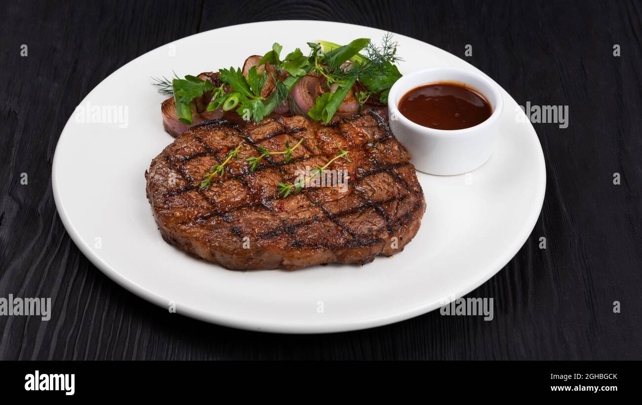 Steak Angus noir grillé sur plaque blanche sur fond de bois noir Banque D'Images