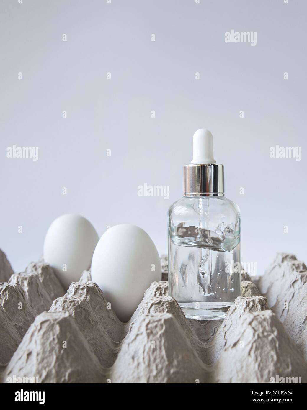 Une bouteille de verre de sérum de face d'oeuf se trouve sur une boîte d'oeufs avec plusieurs oeufs près sur le fond blanc. Ton naturel tendance. Banque D'Images
