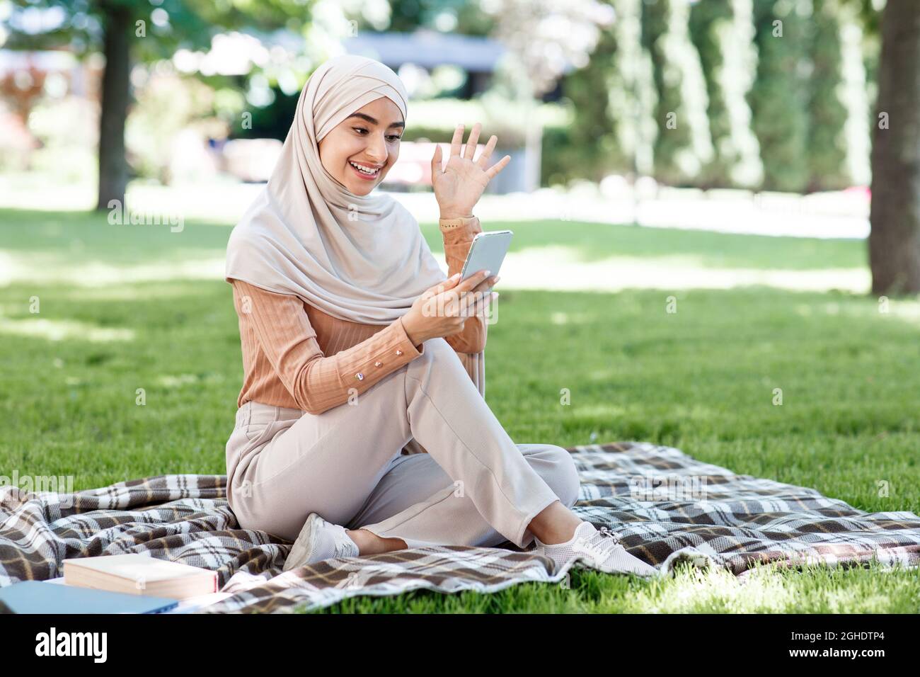 Une jeune femme musulmane arabe heureuse dans le hijab appelle sur un smartphone, réunion vidéo dans le parc vert Banque D'Images