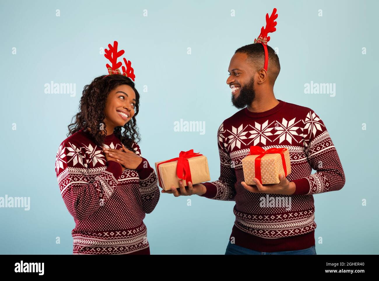 Mari noir donnant un cadeau de Noël à une dame heureuse, célébrant ensemble Noël, debout sur fond bleu Banque D'Images