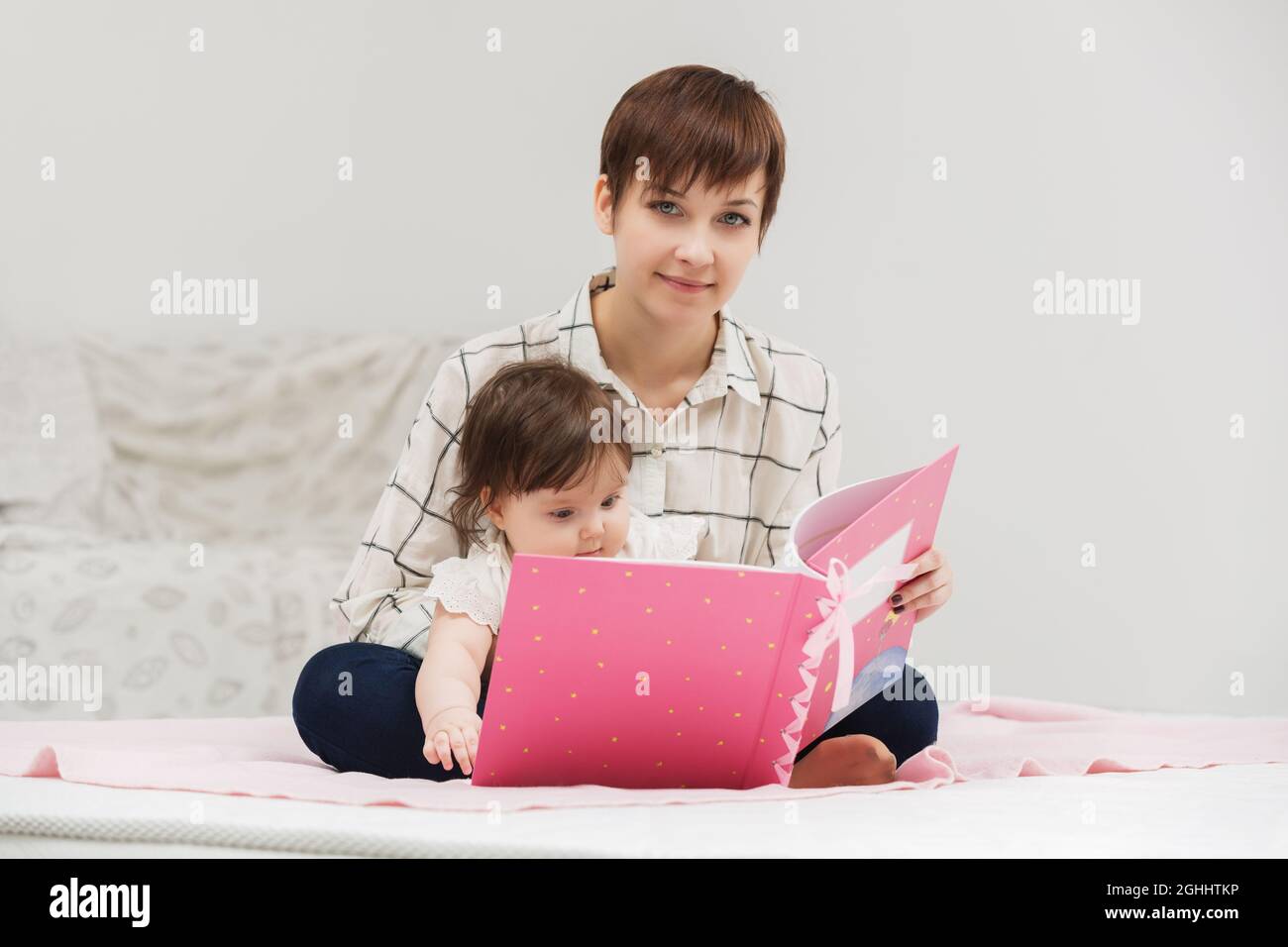 Heureux jeune mère et little baby girl reading a book on bed Banque D'Images