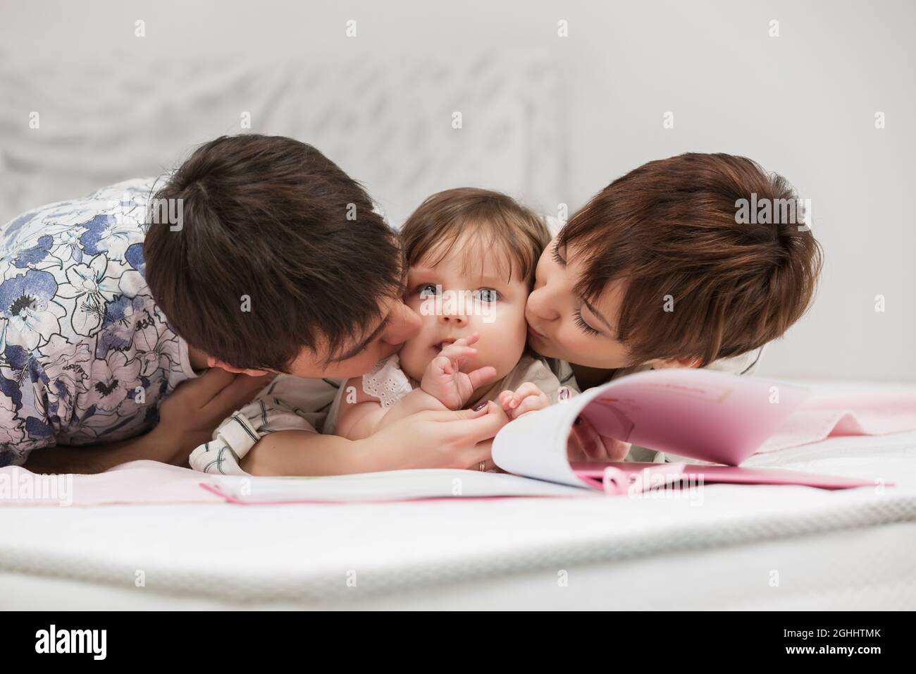 Une jeune famille heureuse avec une petite fille qui lit un livre sur le lit Banque D'Images