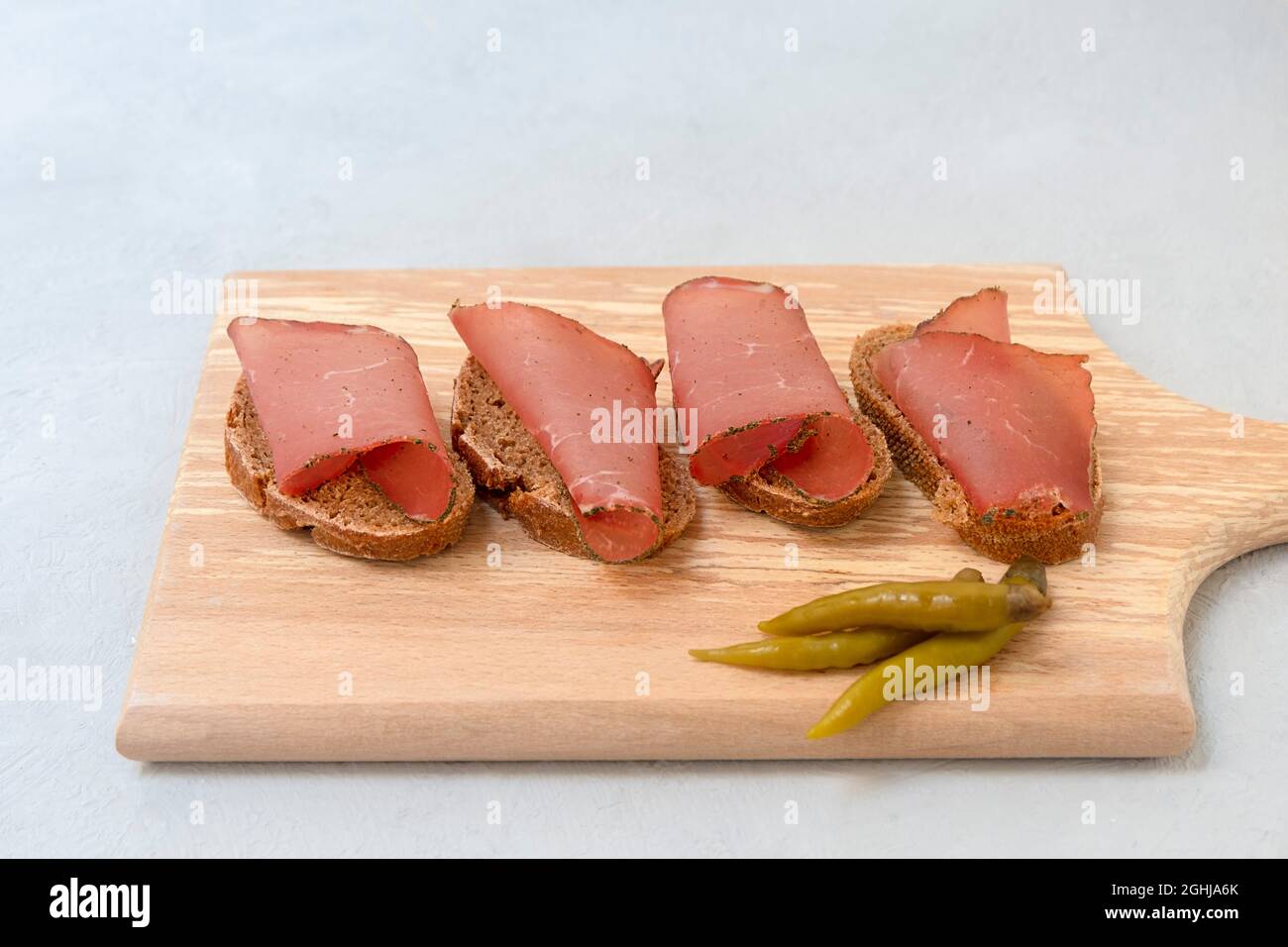 Sandwich avec des tranches de viande séchée servi sur planche à découper sur fond gris neutre Banque D'Images