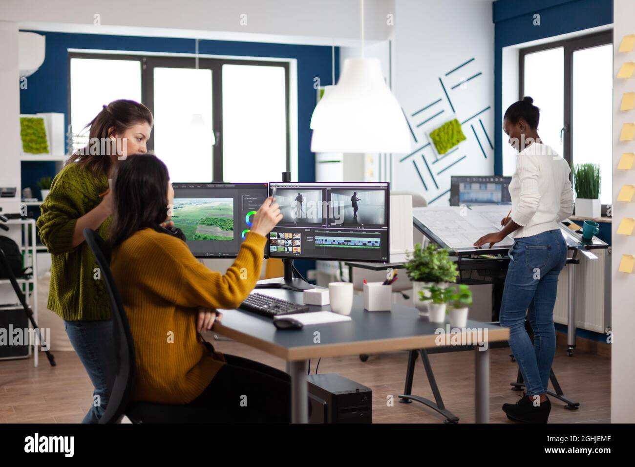 Collègues parlant de projet de film regardant des films travaillant dans le bureau d'agence de création avec deux moniteurs. Les vidéastes traitent le montage vidéo avec un logiciel de post-production Banque D'Images