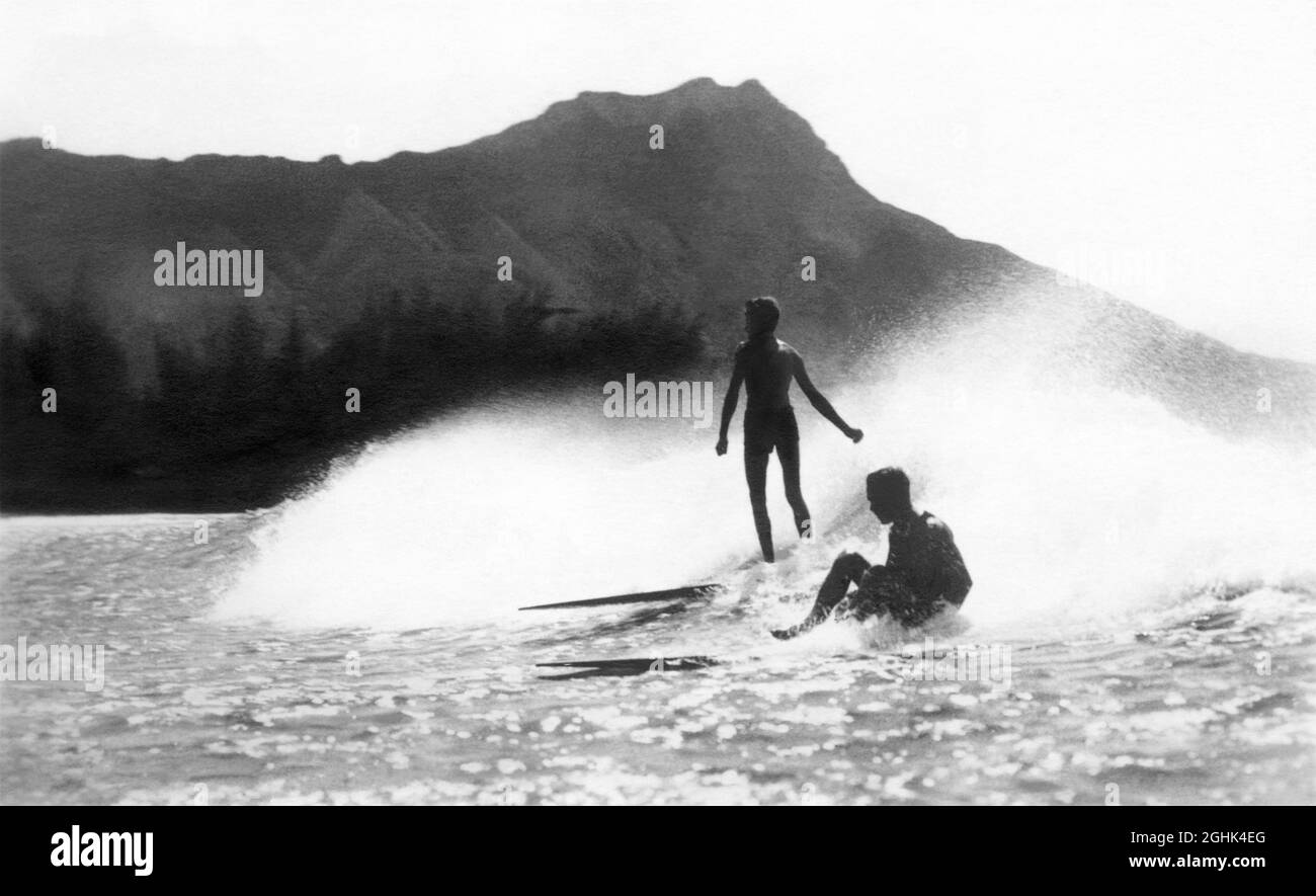 Début du XXe siècle, photo de surf vintage des surfeurs qui surfent sur une vague sur des planches de surf en bois à Waikiki, Honolulu, territoire d'Hawaï, avec Diamond Head en arrière-plan. (Photo de Roscoe Perkins, c1916.) Banque D'Images
