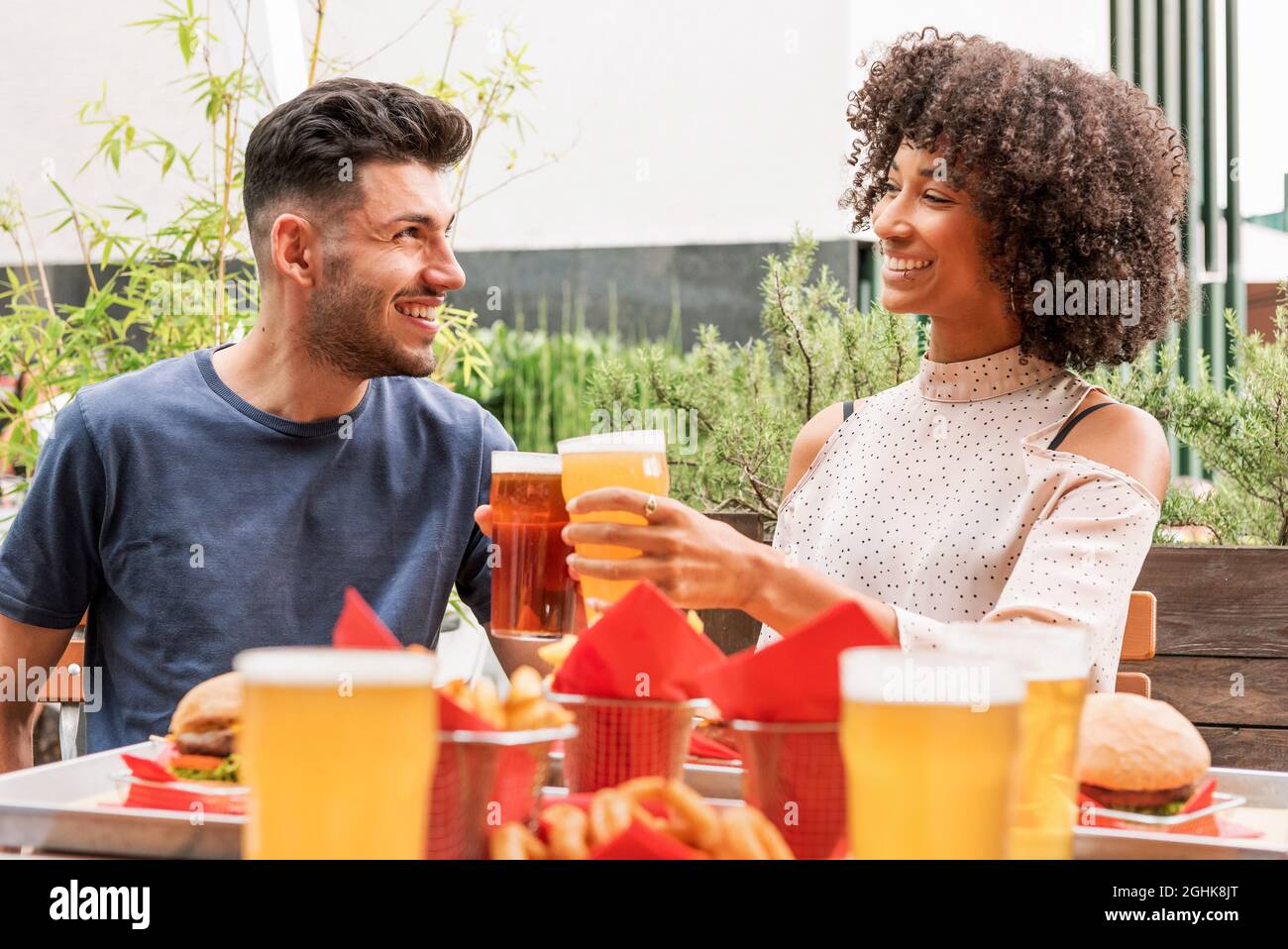 Joyeux jeune couple multiracial se trinquer des verres de bière tout en appréciant le week-end d'été ensemble dans le restaurant en plein air et en célébrant les vacances Banque D'Images