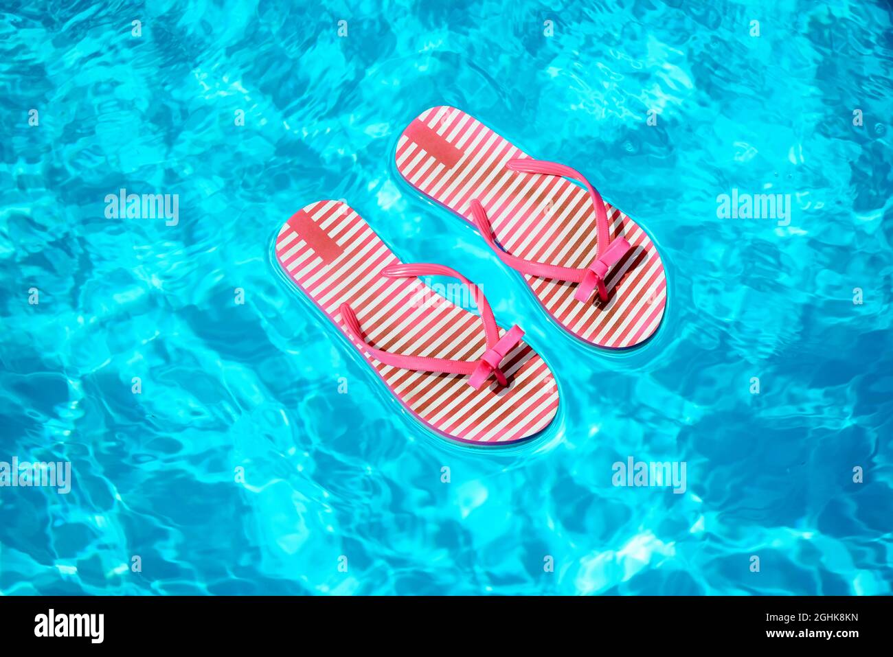 Paire de tongs à rayures rouges et blanches flottant sur l'eau bleue dans une piscine étincelante baignée de soleil en été Banque D'Images