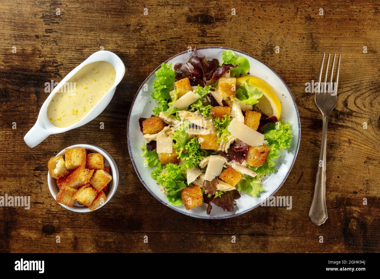Salade César au poulet, plan plat avec sauce classique à base de mayonnaise et croûtons, sur fond de bois rustique foncé Banque D'Images