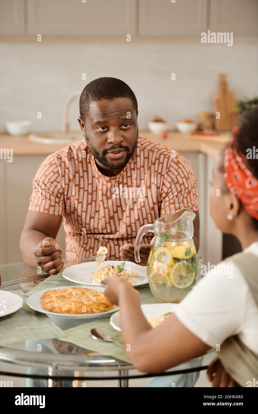 Un jeune homme africain parle à sa femme tout en mangeant des pâtes à table servie au dîner Banque D'Images