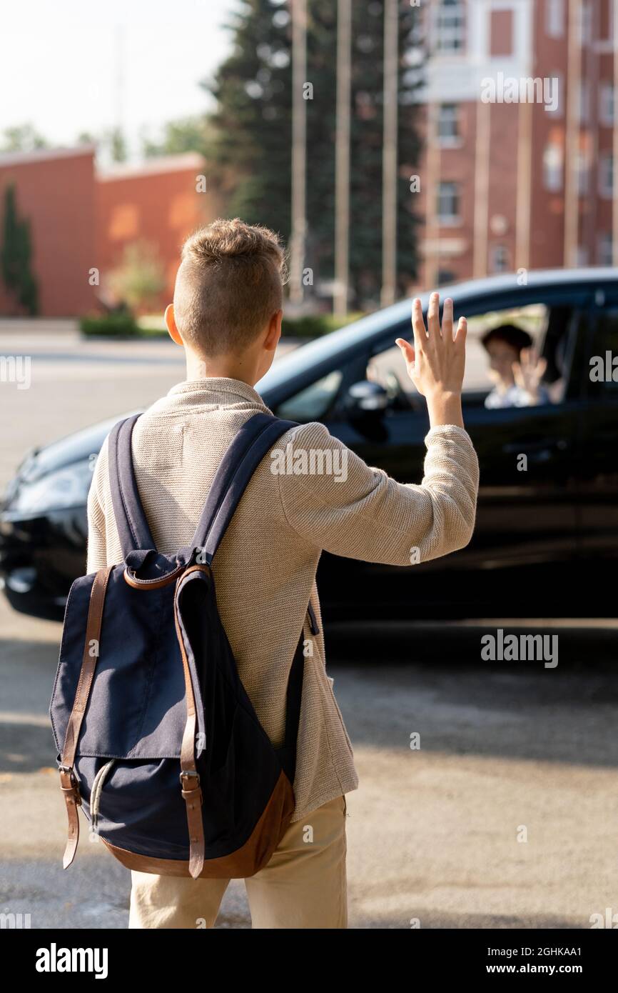 Vue arrière d'un écolier contemporain avec sac à dos et main dans la voiture de ses parents Banque D'Images