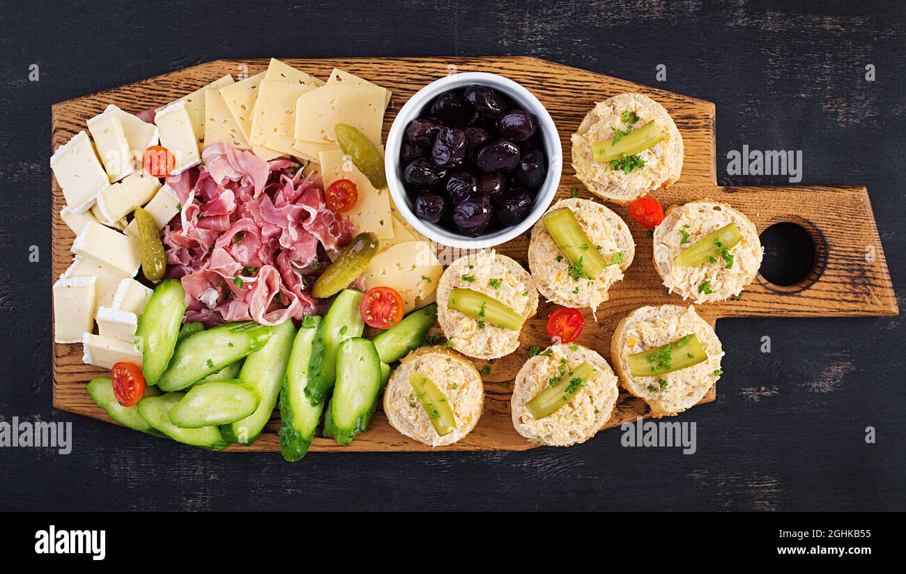 Plateau de restauration antipasti avec jamon, fromage, canape et olives noires sur une planche en bois. Vue de dessus, au-dessus de la tête Banque D'Images