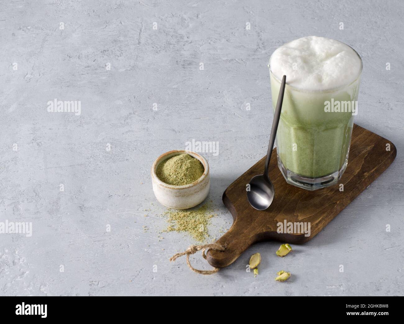 Buvez le latte de café Matcha dans un verre sur un panneau de bois avec une cuillère à café sur fond de béton. Le concept de boissons végétariennes saines Banque D'Images