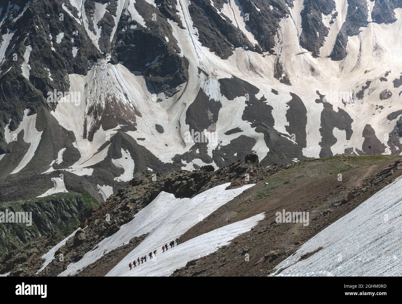Un groupe de randonneurs avec des sacs à dos se promènent le long d'une chaîne de montagnes sur fond de montagnes enneigées. Le concept de voyage à la mountai Banque D'Images