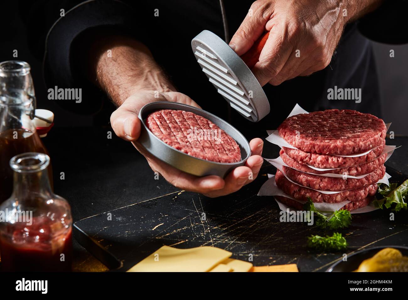 Chef utilisant une presse à hamburger pour préparer des viandes fraîches de bœuf haché maison dans un restaurant à emporter en gros plan sur ses mains et l'ustensile Banque D'Images