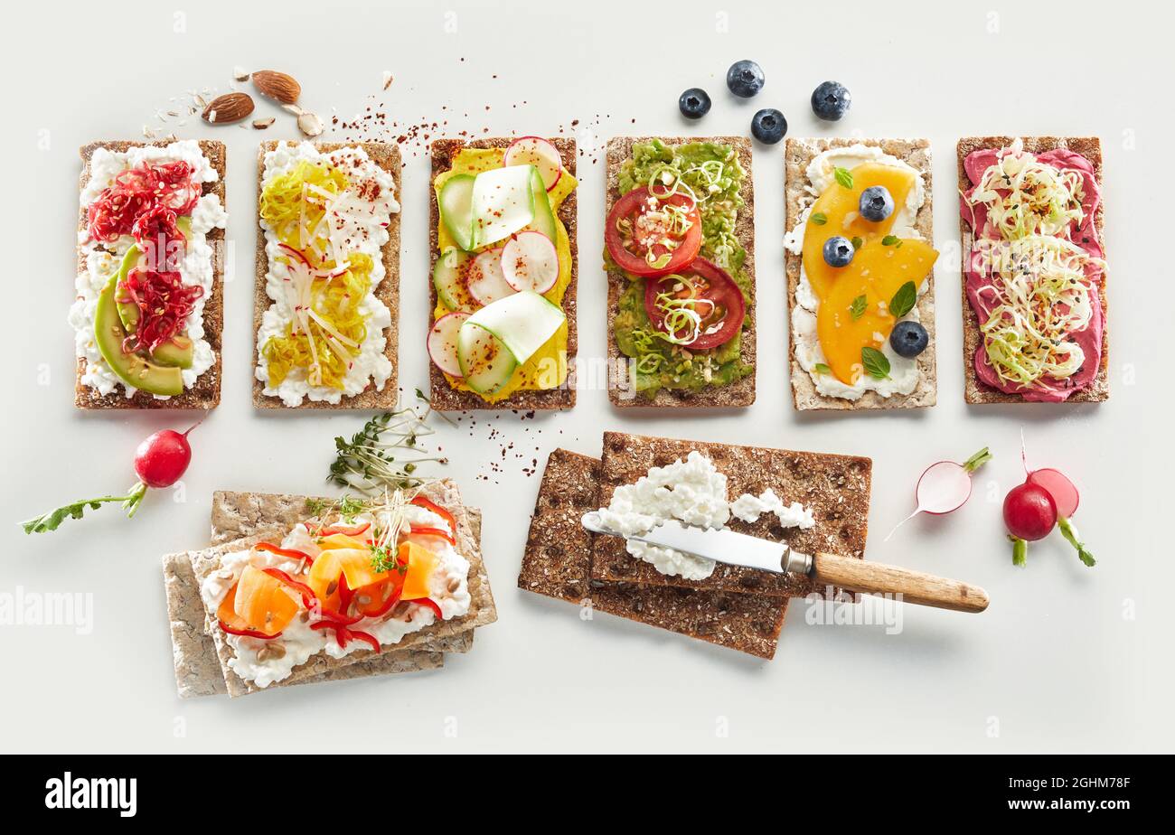 Vue de dessus de l'arrangement des toasts de pain croustillant avec des fruits frais et des légumes assortis placés sur fond blanc pour les repas végétariens santé Banque D'Images