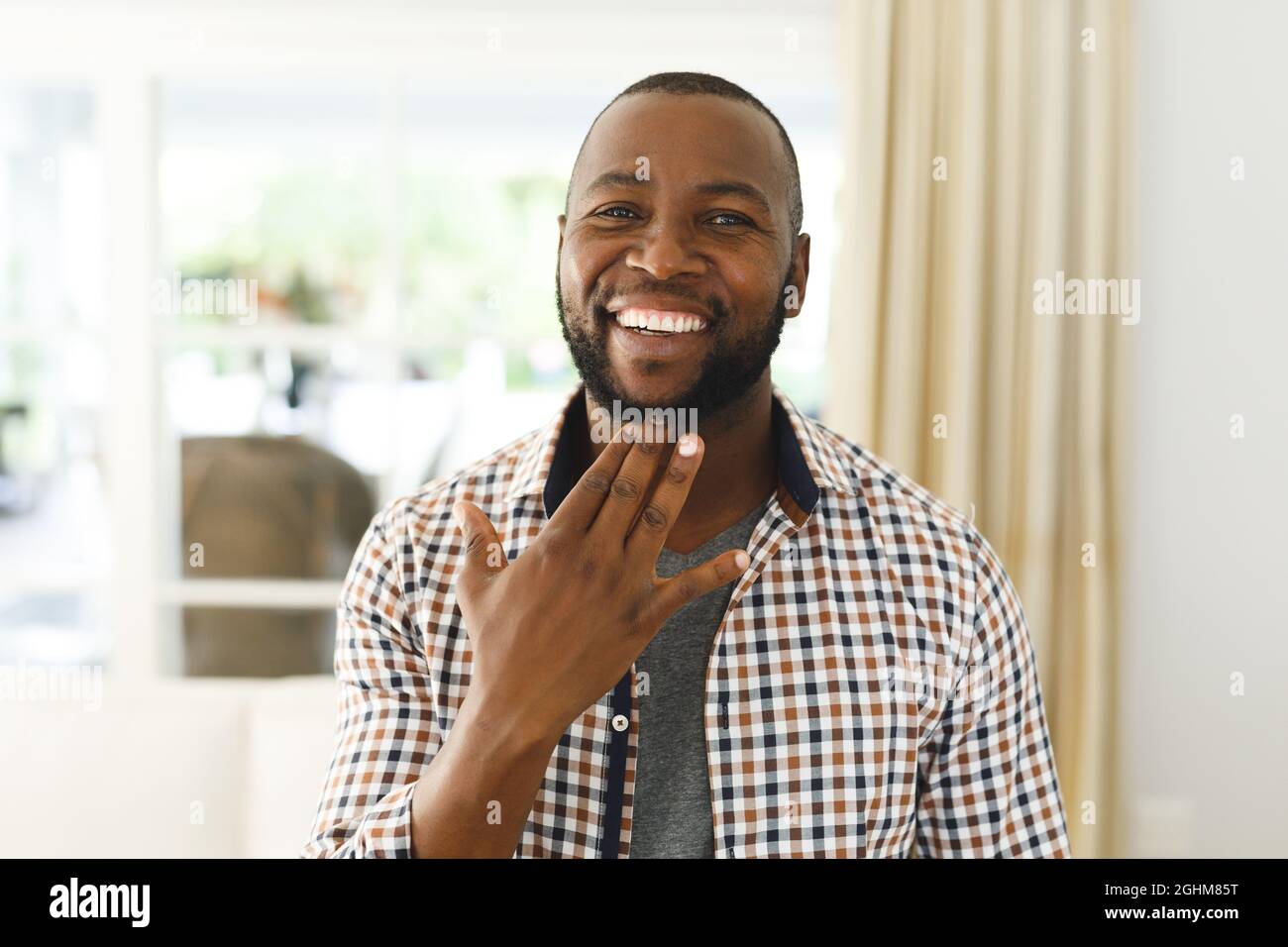 Portrait de l'homme afro-américain souriant et regardant l'appareil photo dans le salon parlant langue des signes Banque D'Images