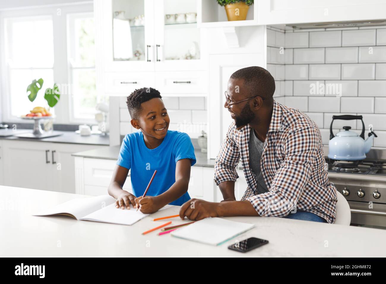 Joyeux père et fils afro-américains dans la cuisine, faisant les devoirs ensemble Banque D'Images