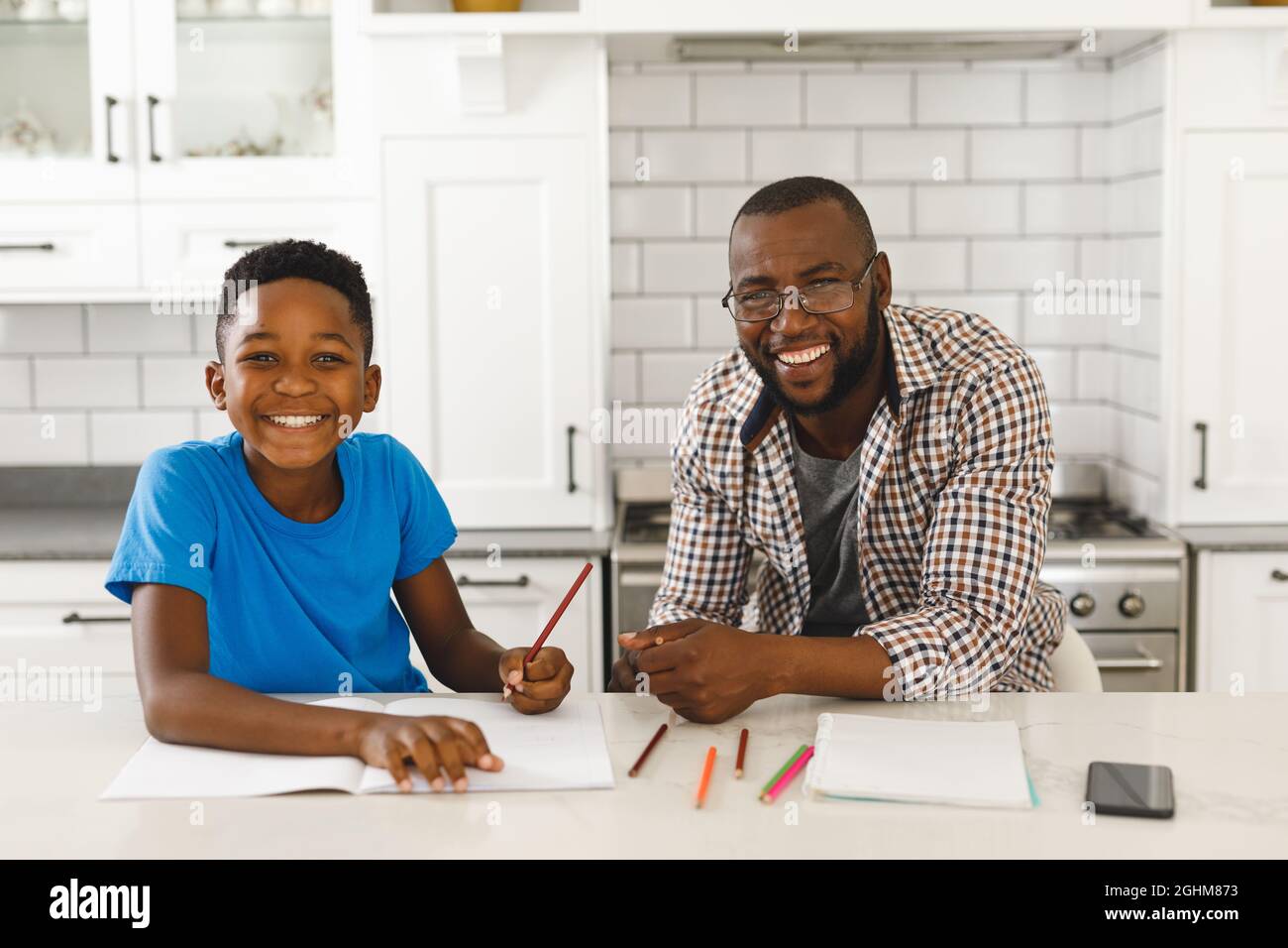 Portrait d'un père afro-américain souriant et de son fils dans la cuisine, faisant les devoirs ensemble Banque D'Images