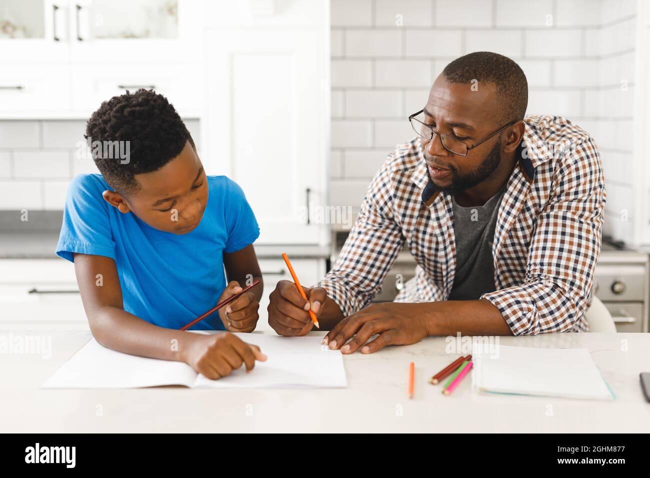 Père afro-américain et son fils en cuisine, faisant leurs devoirs ensemble Banque D'Images