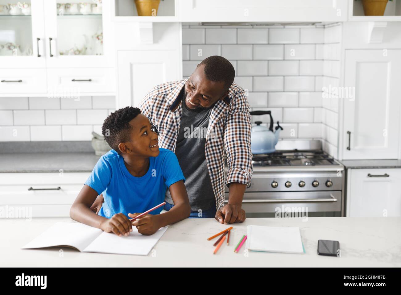 Souriant père afro-américain et son fils dans la cuisine, faisant les devoirs ensemble Banque D'Images