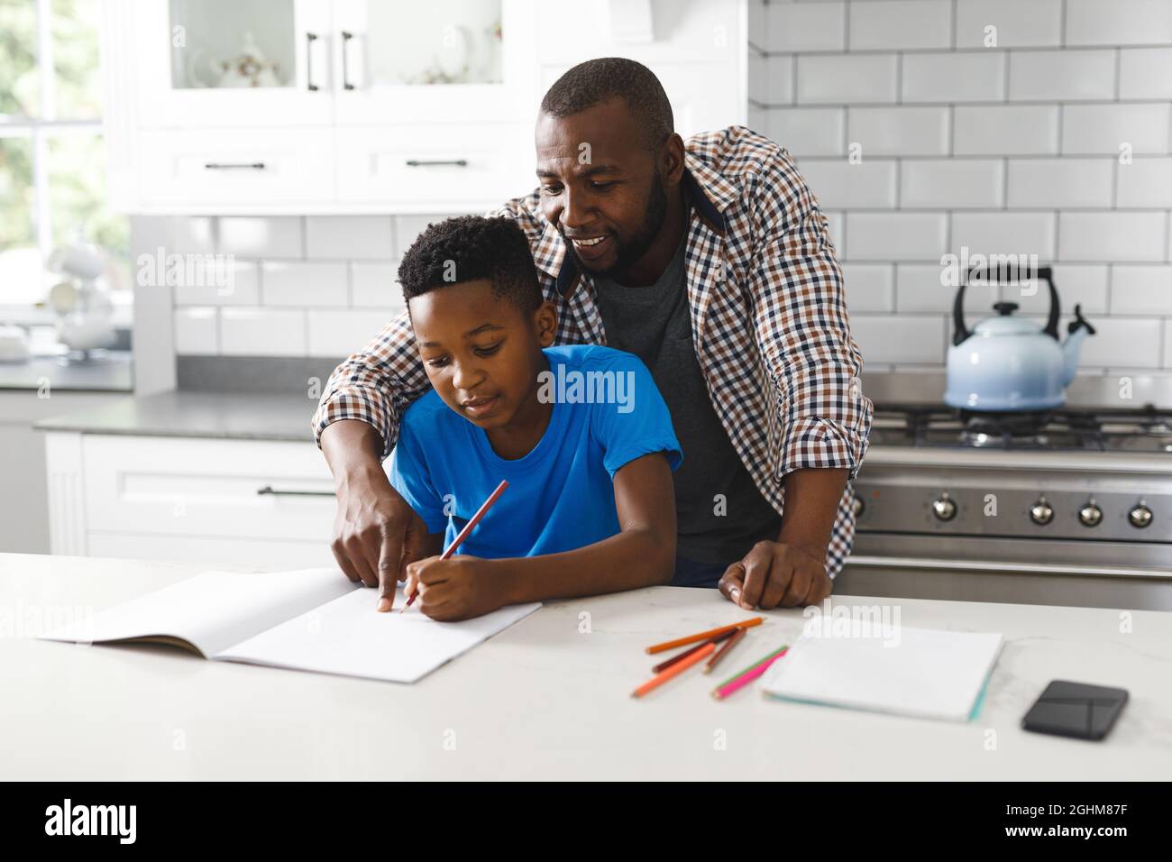 Souriant père afro-américain et son fils dans la cuisine, faisant les devoirs ensemble Banque D'Images