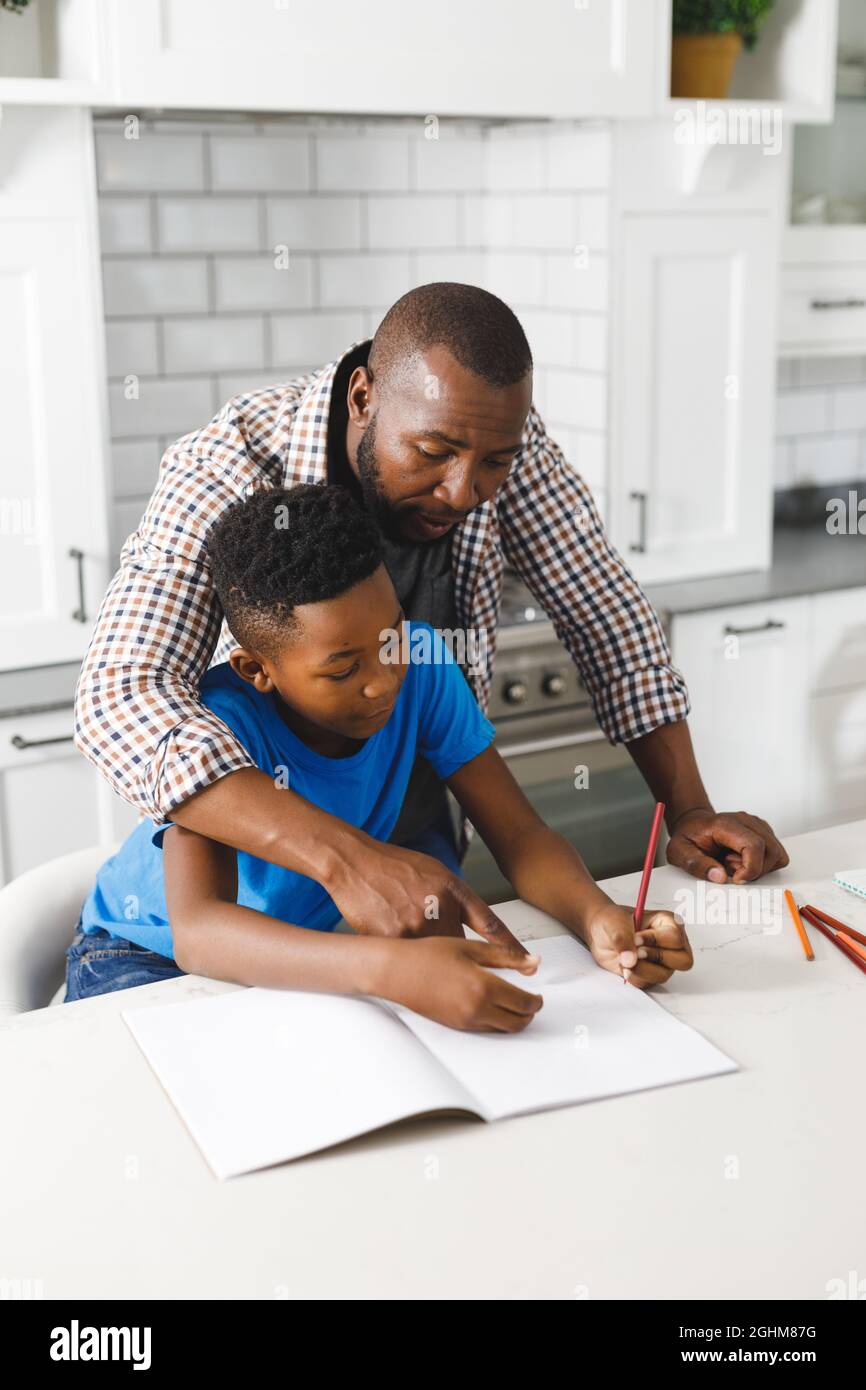 Père afro-américain et son fils en cuisine, faisant leurs devoirs ensemble Banque D'Images
